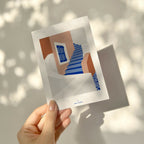 Carte illustrée tenue par une main, escaliers bleus et façade brun/orange