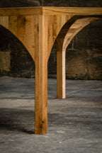 Piètement de table en bois avec double arc ajouré, gros plan.