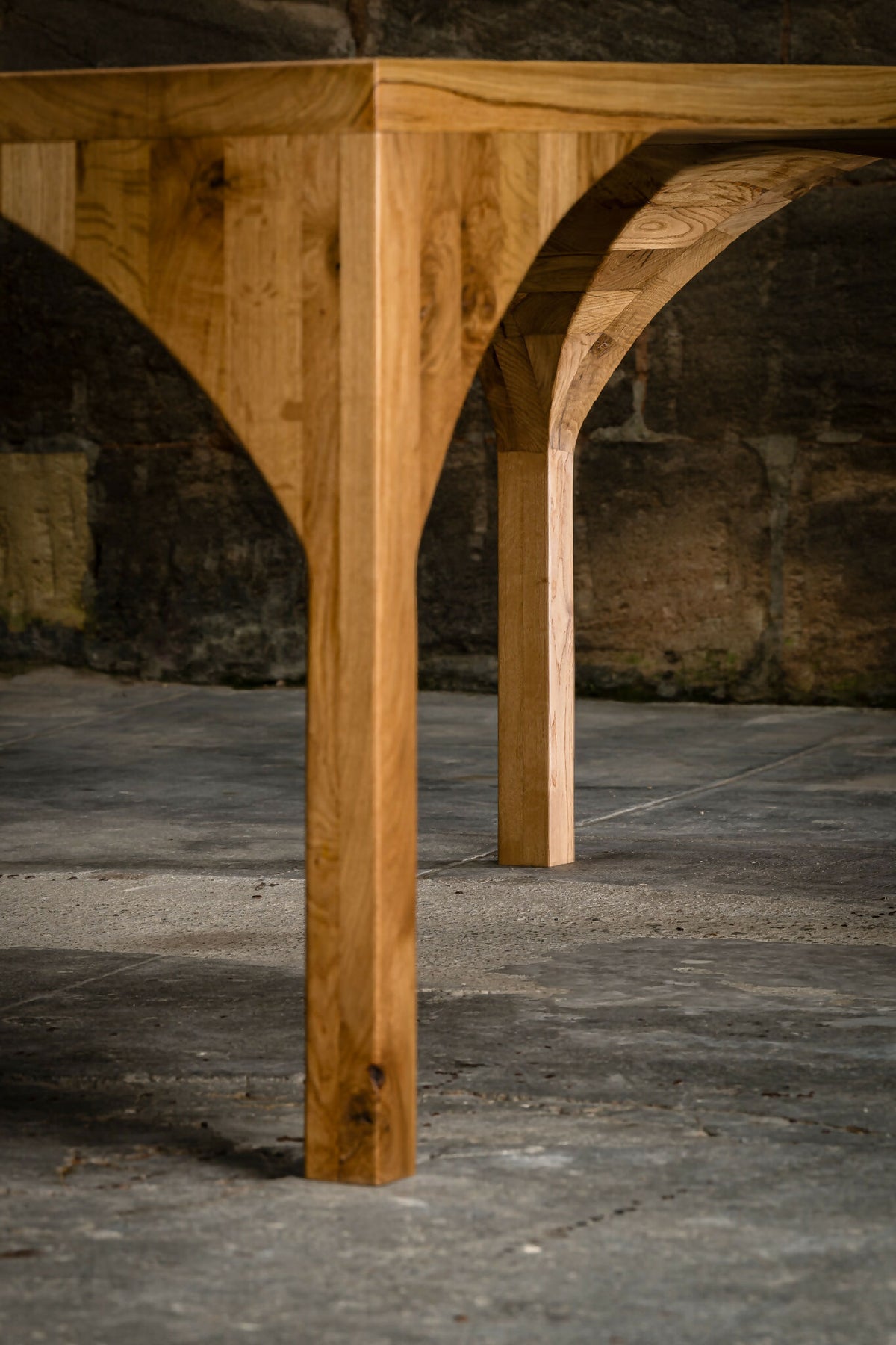 Piètement de table en bois avec double arc ajouré, gros plan.