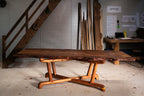 Table en bois massif avec plateau rustique et piètement en tréteaux arrondis.
