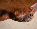 Table en bois massif, détail sculpté avec nœud et textures sombres du bois.
