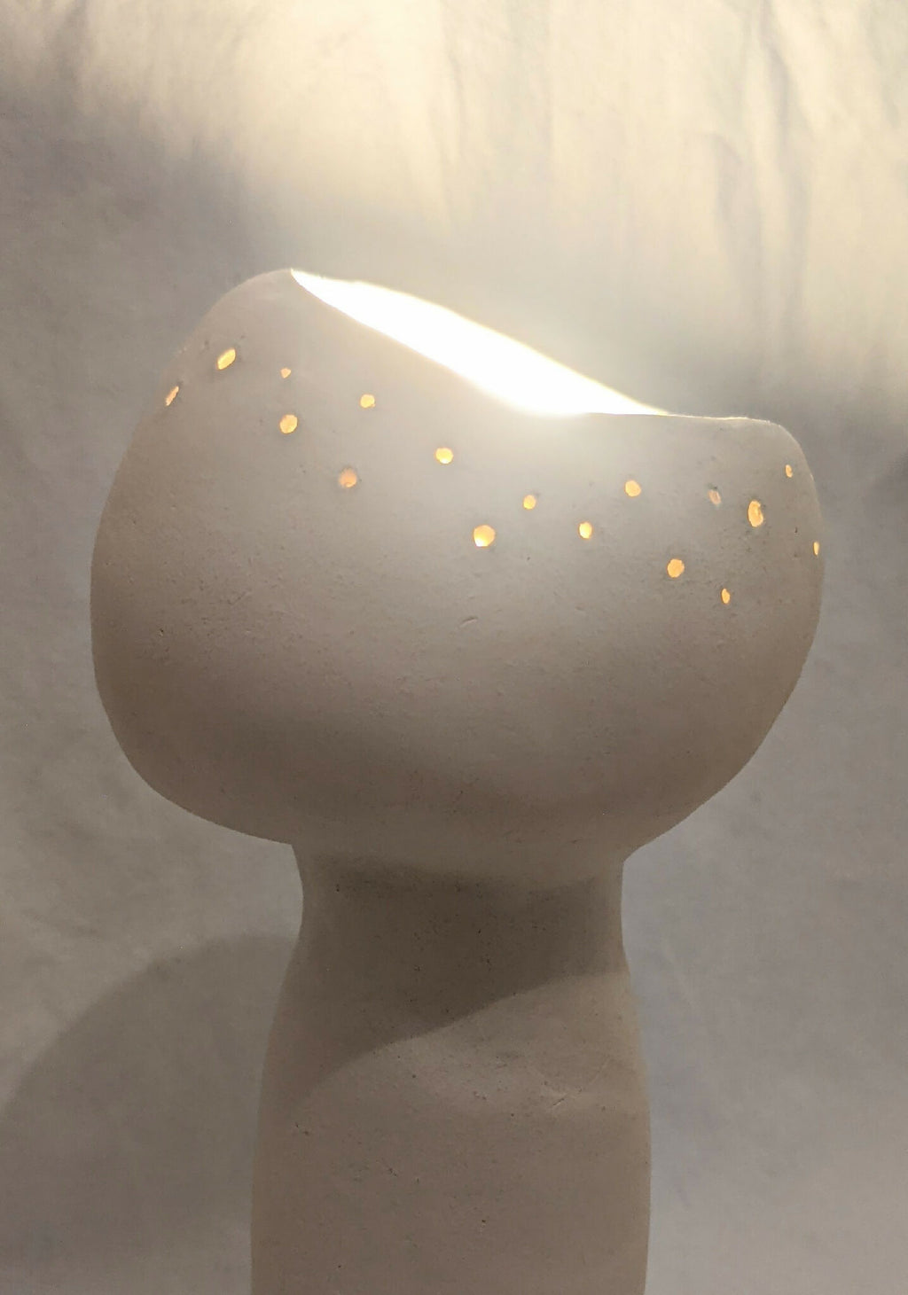 Lampe à poser champignon en céramique, blanc cassé, lumière allumée à travers les trous.