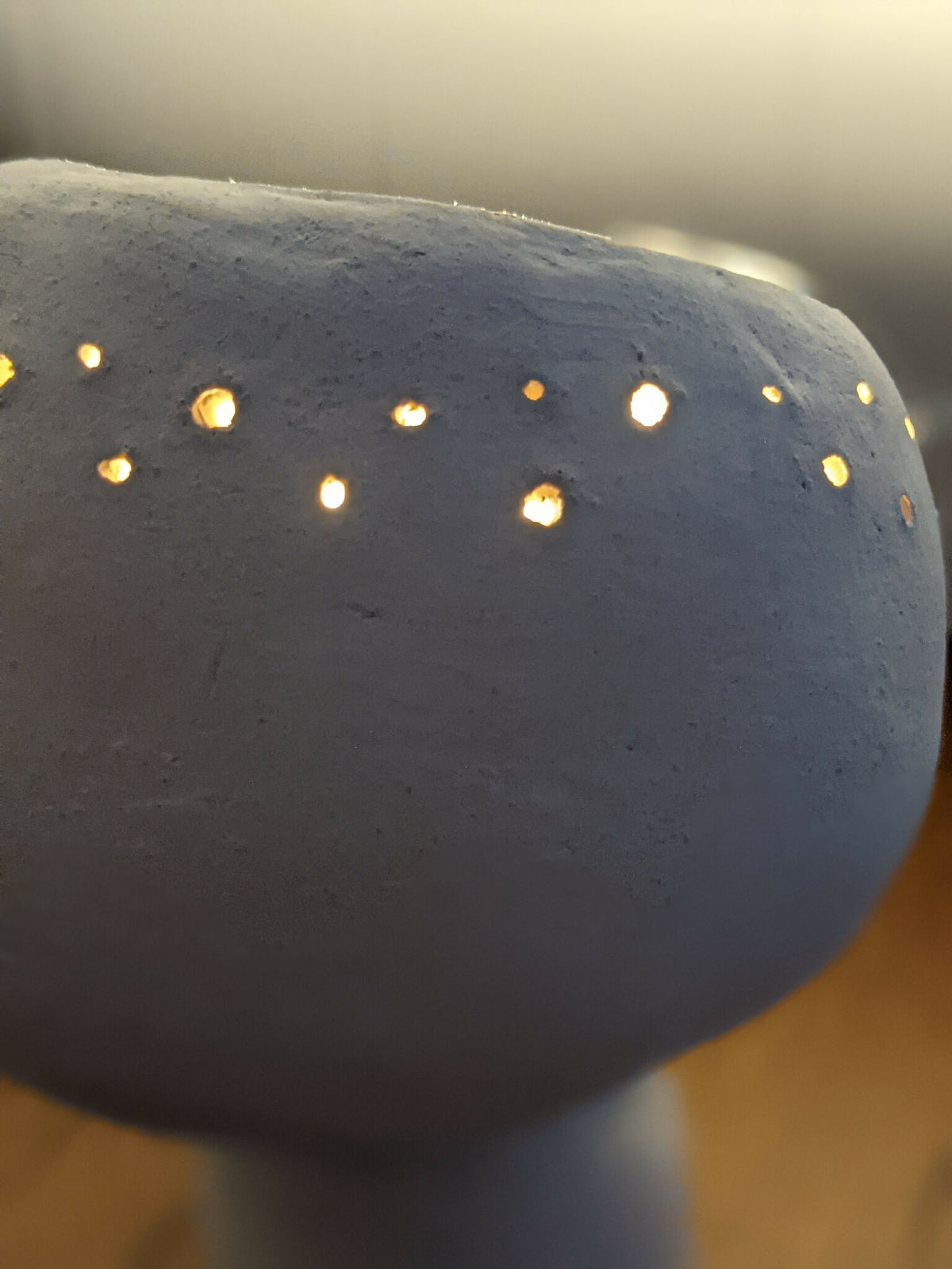 Détail de la lampe en céramique champignon, perforations éclairées, lueur chaude visible.