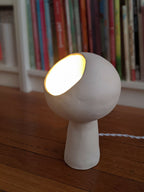 Lampe à poser design blanche, forme sculpturale, lumière allumée, câble visible