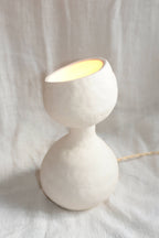 Lampe design blanche en forme de sablier, allumée, câble visible