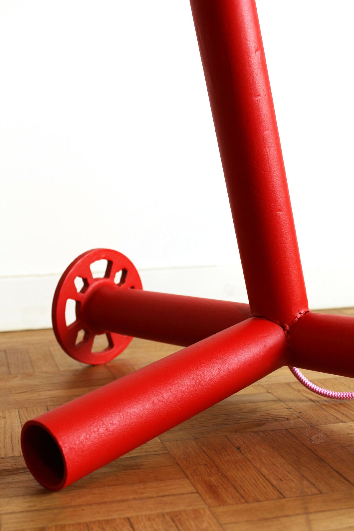 Pied de lampe rouge avec tubes horizontaux et disque de fixation, sol en bois