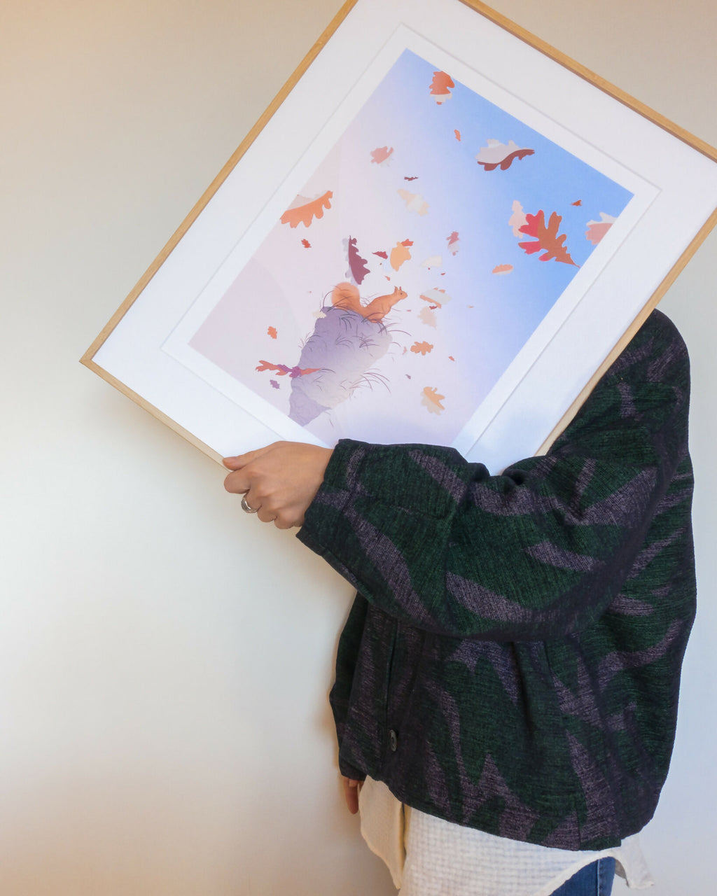 Affiche dans un cadre blanc, tenue par une main, avec chat et feuilles colorées.