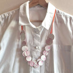Collier en disques ronds blancs, gris et roses à motifs, sur chemise blanche