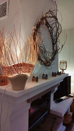 Luminaire en rotin brun tressé sur pot en grès, lumière chaude à l’intérieur.