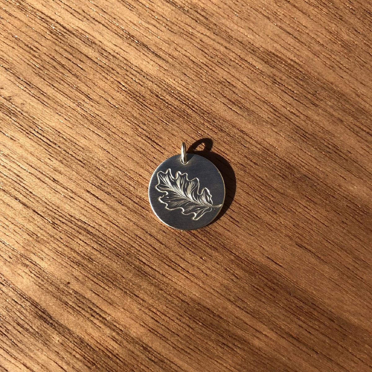 Médaille feuille de chêne en argent 925, forme ronde, bélière visible au sommet.