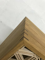 Angle supérieur d’une vitrine en chêne, assemblage en bois et motif ajouré en arrière-plan.