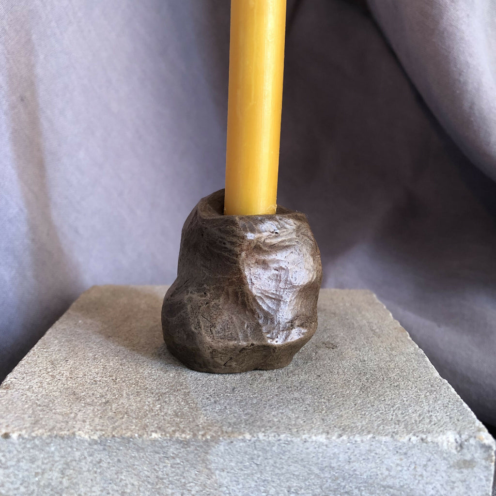 Mini bougeoir en pierre sombre avec bougie jaune, base sur socle.