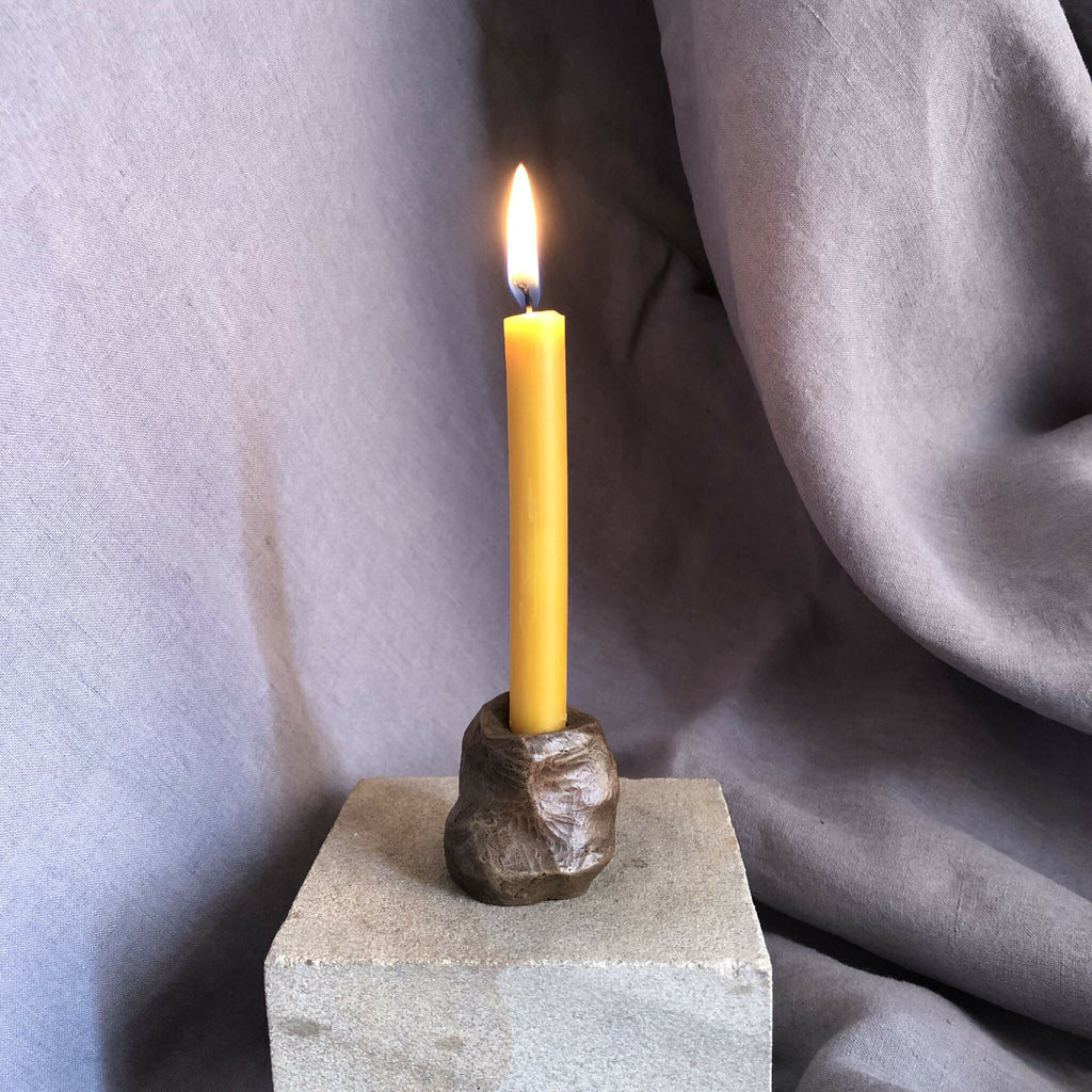 Mini bougeoir en pierre sombre avec bougie jaune allumée, socle rectangulaire.