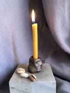Mini bougeoir en pierre sombre avec bougie allumée et coquillages décoratifs.