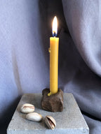 Mini bougeoir en pierre sombre avec bougie allumée, coquillages près du socle.