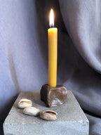 Mini bougeoir en pierre sombre, bougie jaune allumée sur socle texturé avec coquillages