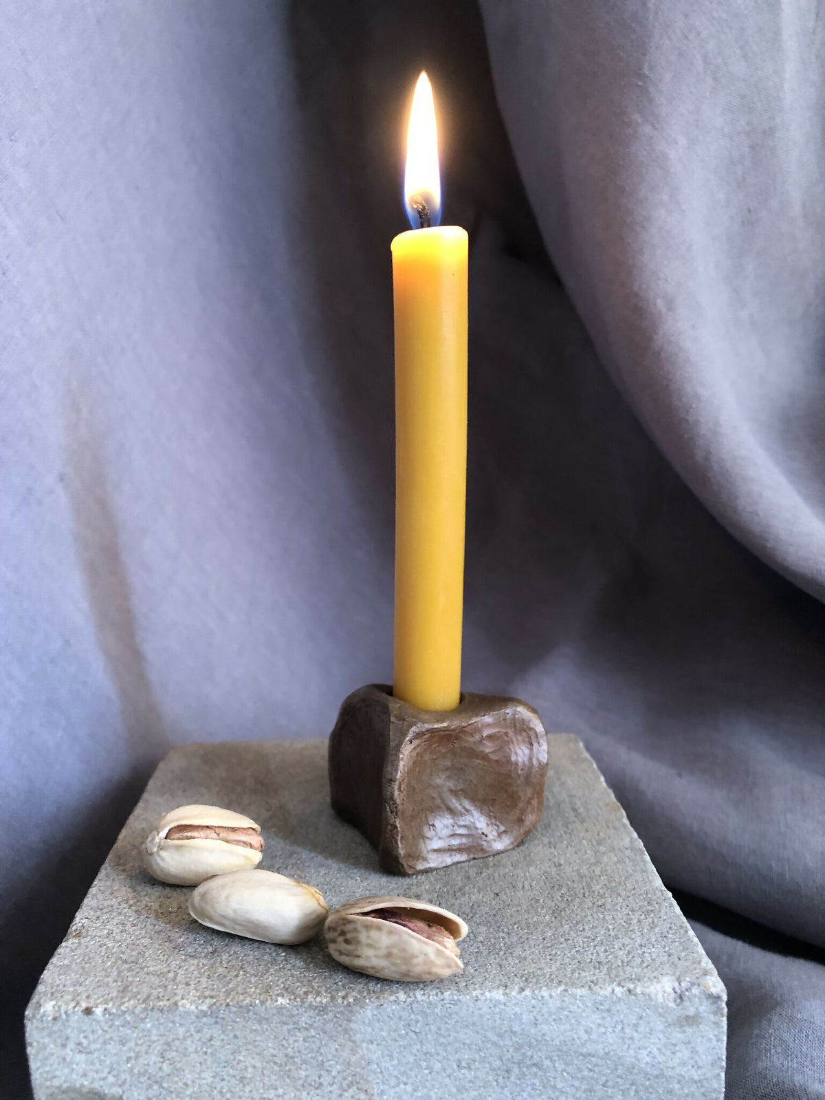 Mini bougeoir en pierre sombre, bougie jaune allumée sur socle texturé avec coquillages