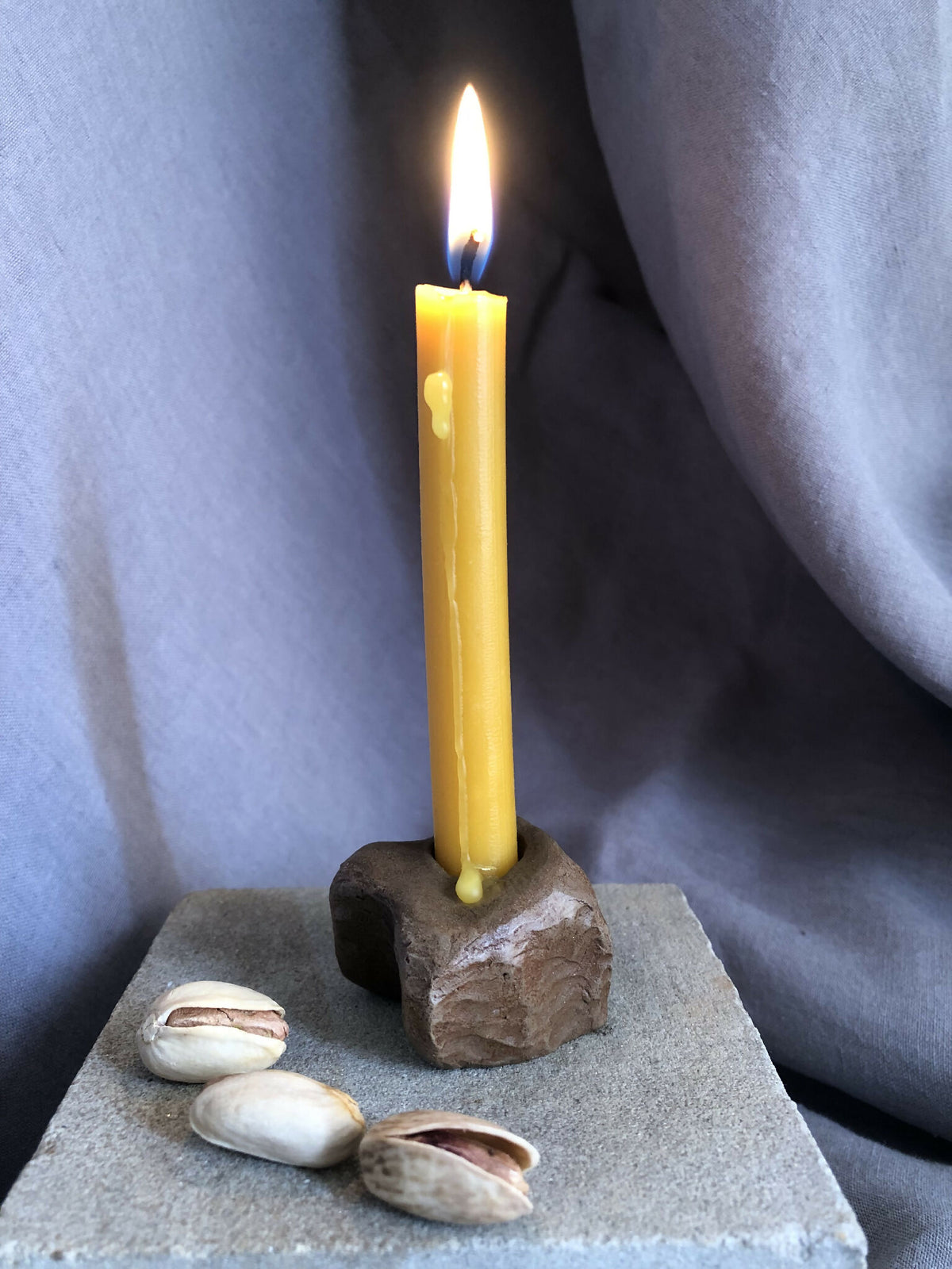 Mini bougeoir en pierre sombre, bougie jaune allumée sur socle carré avec coquillages