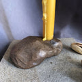 Mini bougeoir en pierre brune avec bougie jaune allumée, tige centrale.
