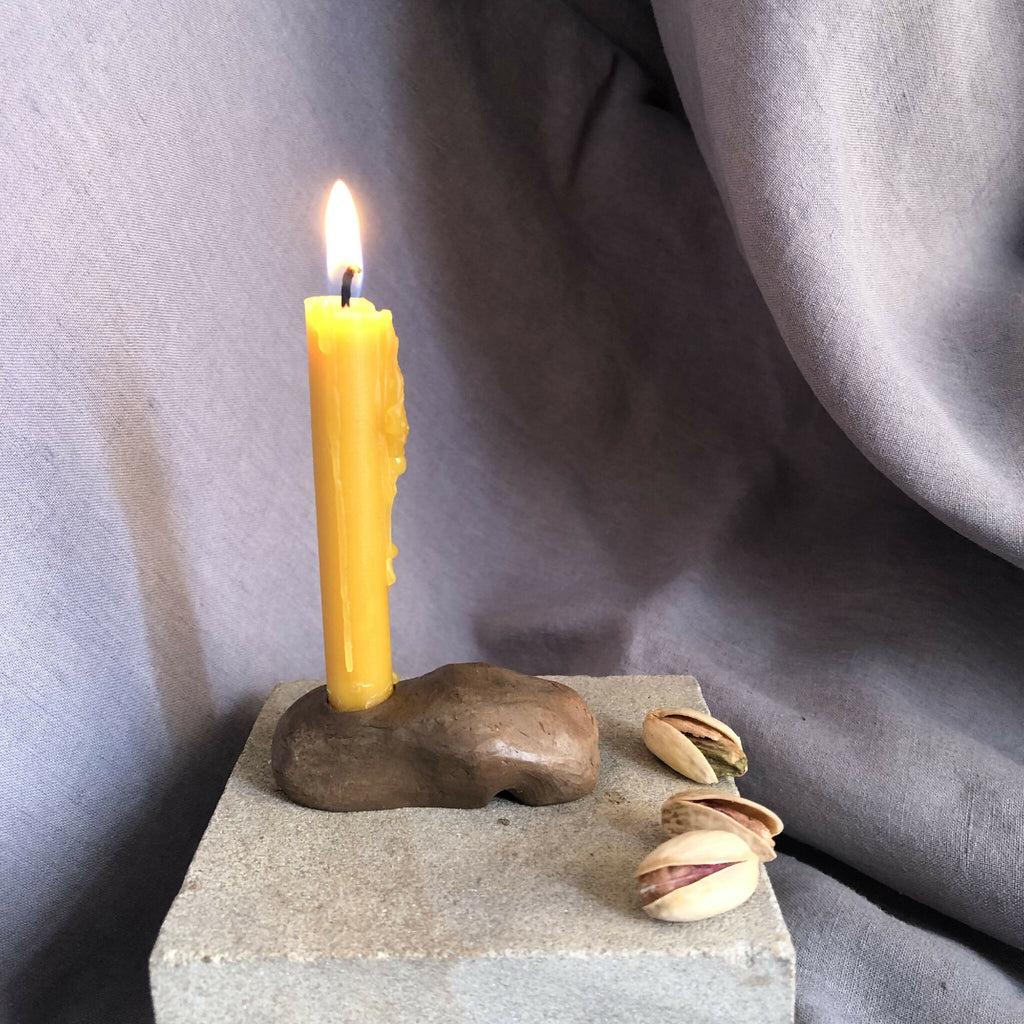 Mini bougeoir sur socle en pierre grise avec bougie jaune, coquillage et galets.