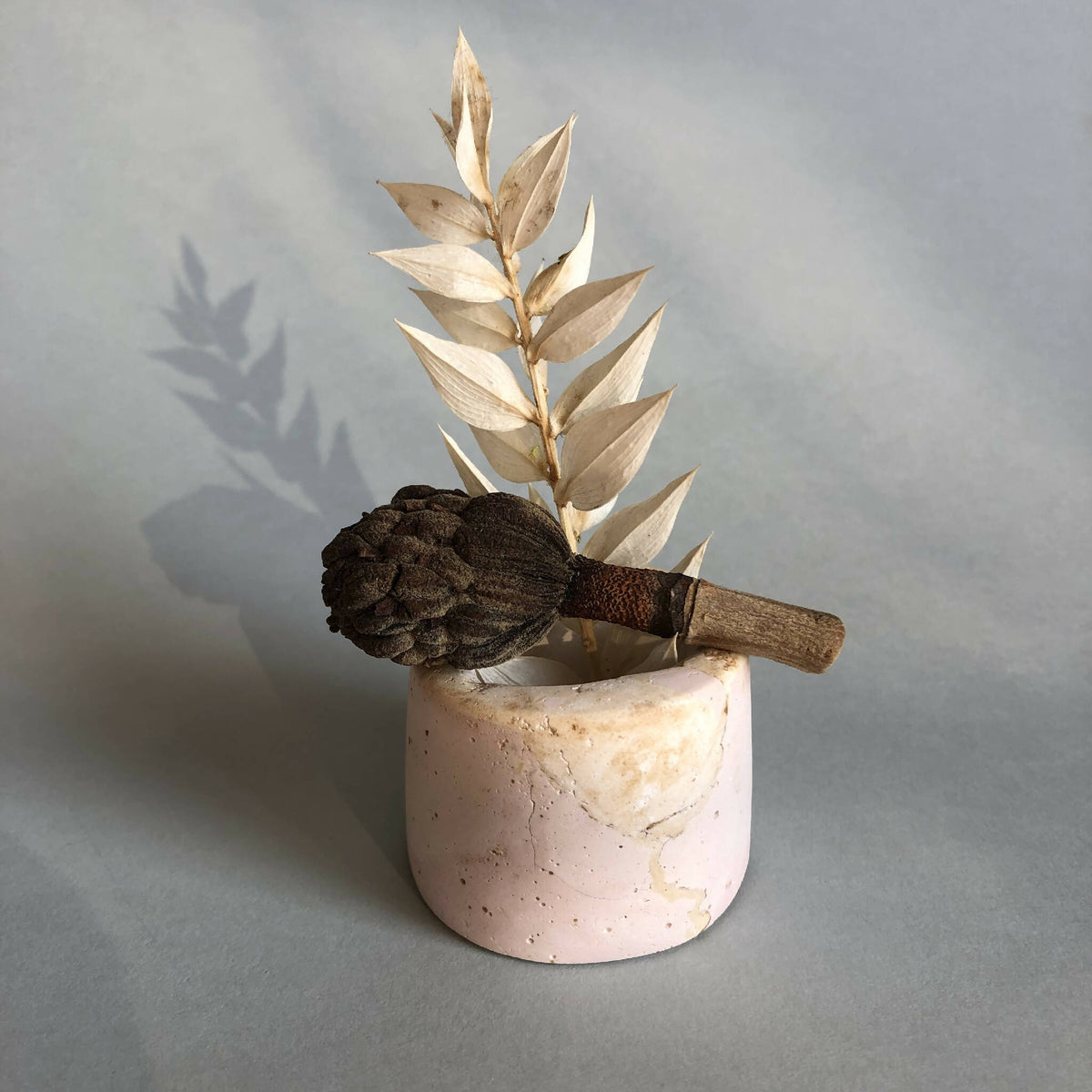 Petit pot en céramique rose pâle avec tige de feuilles dorées et fleur brune