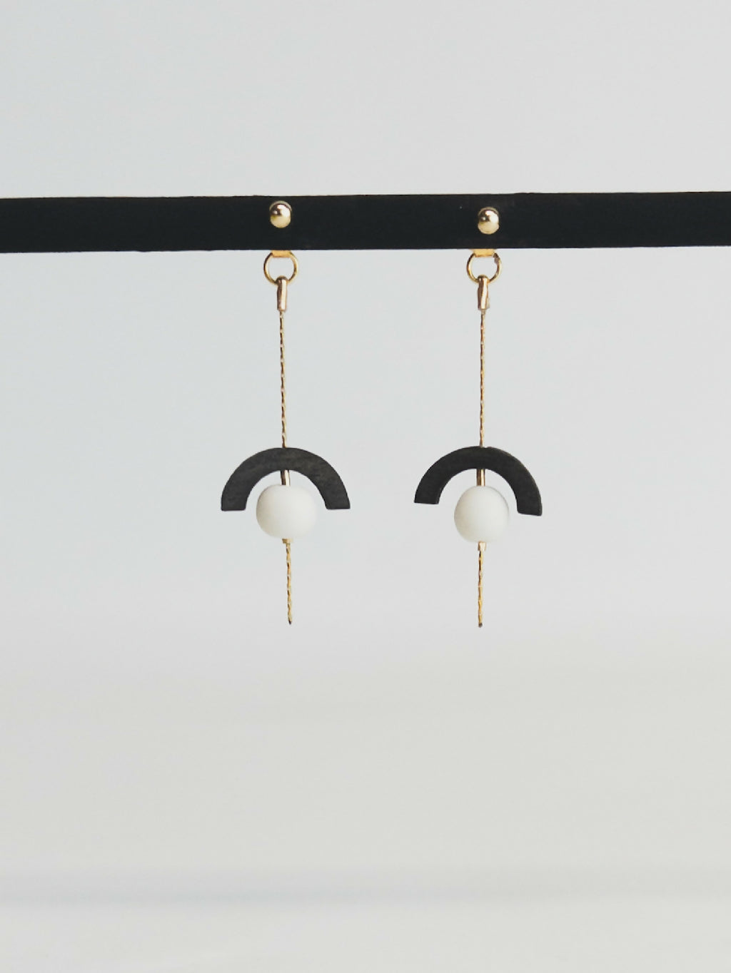 Boucles d’oreilles pendantes : demi-cercle noir, perle blanche, chaînette dorée.