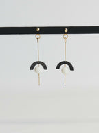 Boucles d’oreilles pendantes : demi-cercle noir, perle blanche, chaînette dorée.