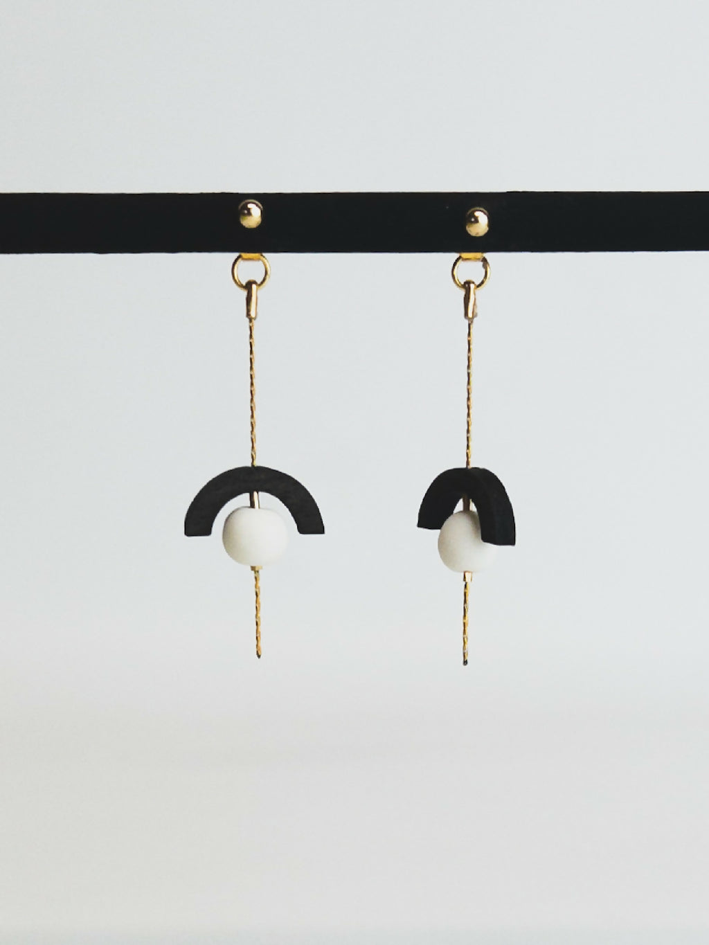 Boucles d’oreilles pendantes avec demi-cercle noir et perle blanche sur chaînette dorée.