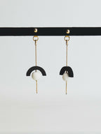 Boucles d’oreilles pendantes avec demi-cercle noir et perle blanche sur chaînette dorée.