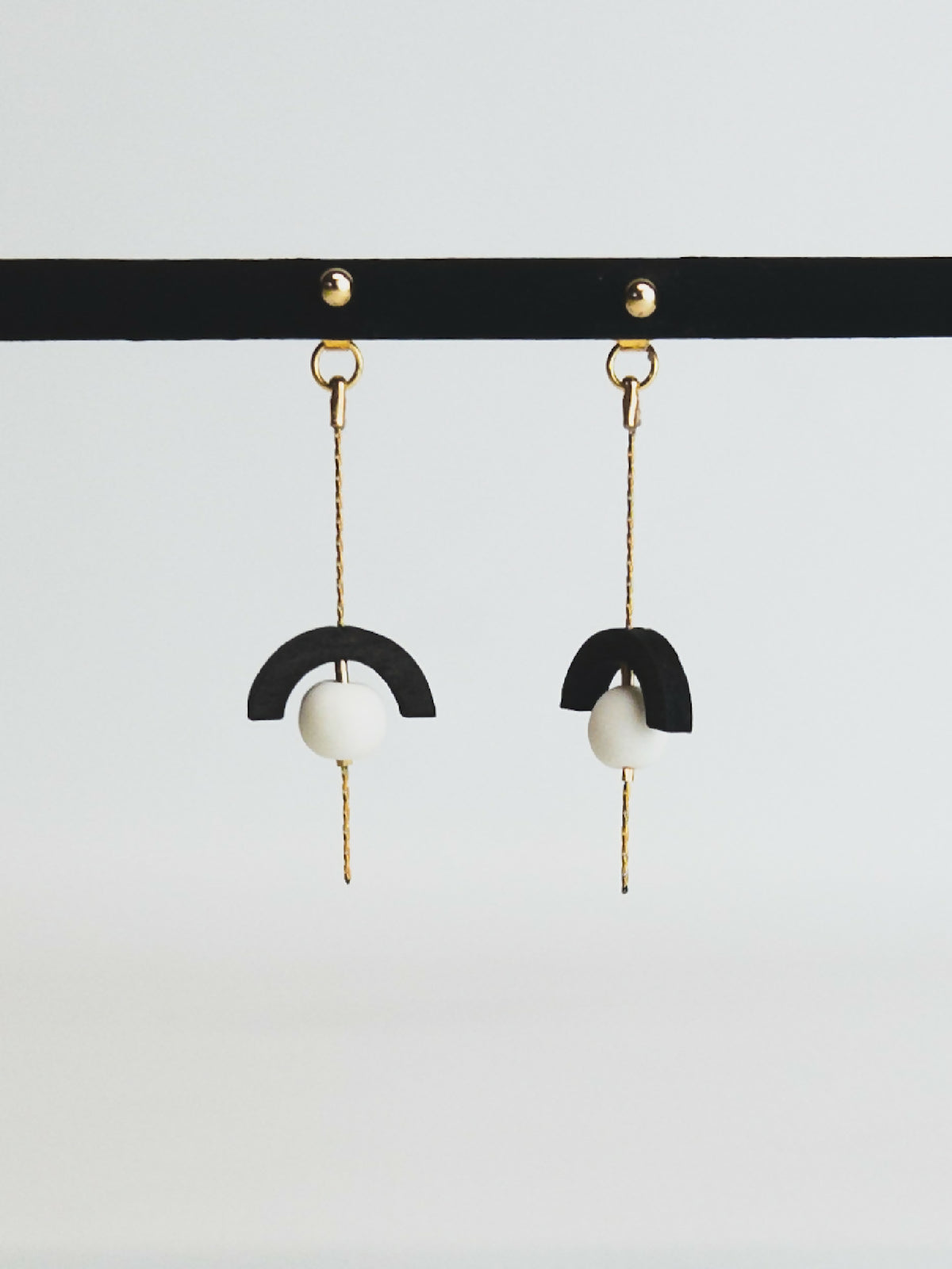 Boucles d’oreilles pendantes avec demi-cercle noir et perle blanche sur chaînette dorée.