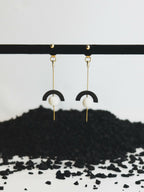 Boucles d’oreilles pendantes : crochet doré, demi-cercle noir et perle blanche.