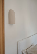 Applique murale beige en céramique sur mur, près d’un lit avec coussins.