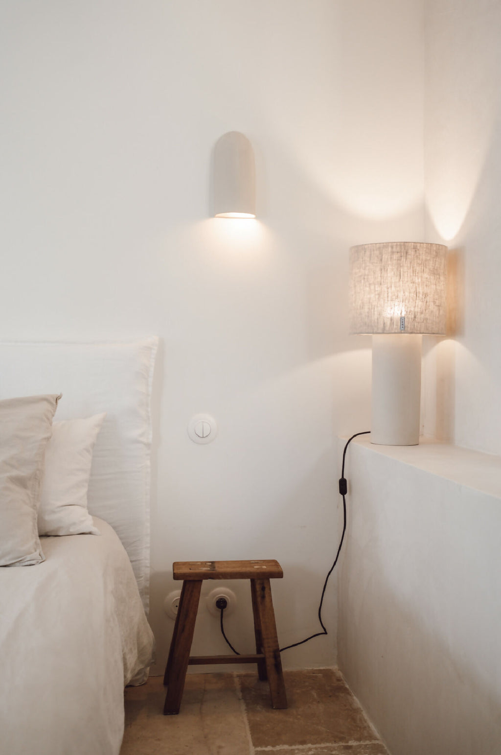 Applique murale beige en céramique avec éclairage chaleureux, près d’une lampe textile.