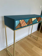 Console avec plateau bleu, structure en bois clair et tiroir à motif losanges bois et bleu.