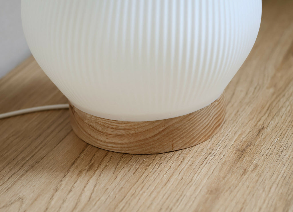 Base en bois strié sous un abat-jour blanc côtelé de lampe d’intérieur.