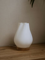 Lampe d’intérieur à abat-jour blanc côtelé avec base en bois, posée sur une étagère.