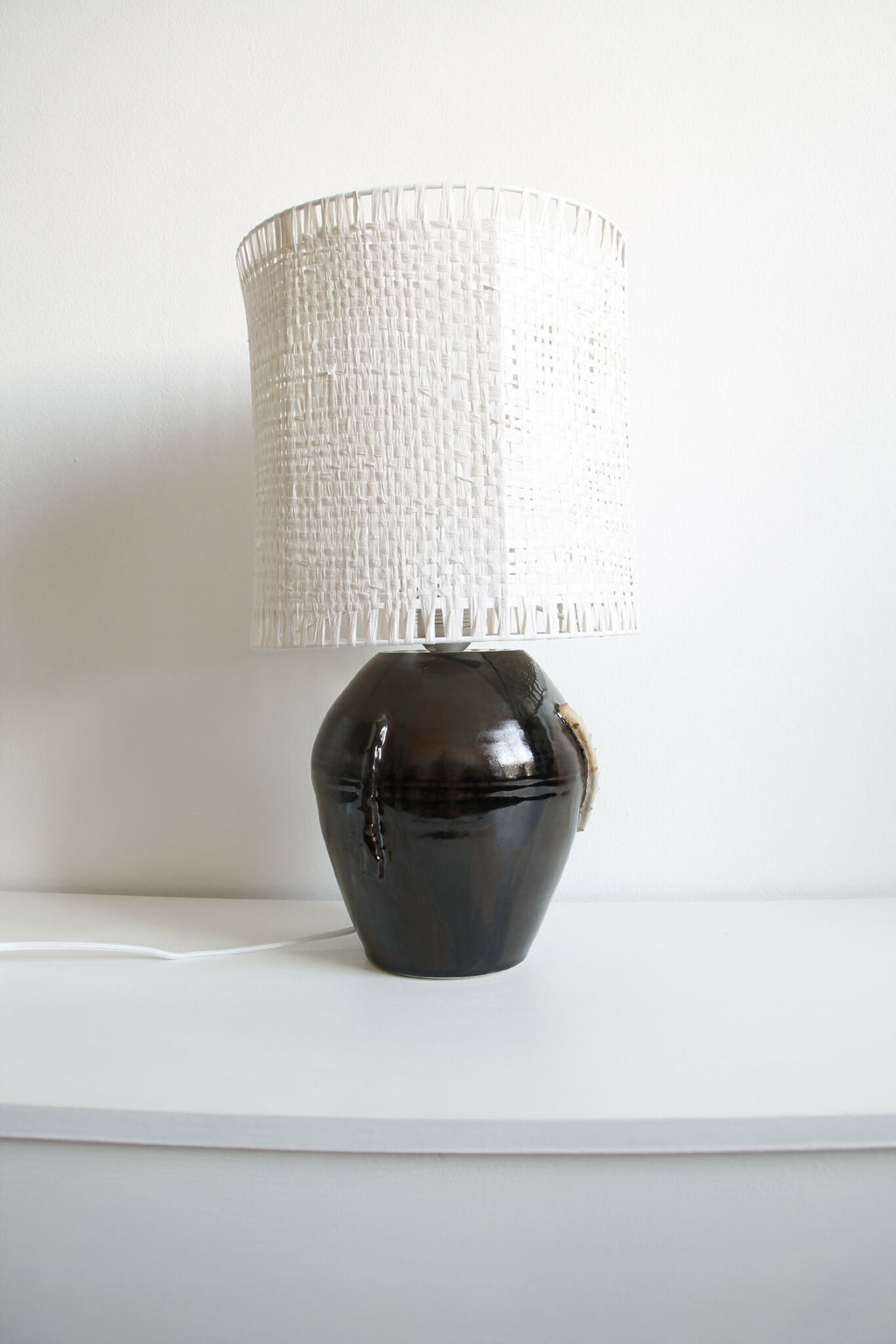 Lampe Puntia sur une table, abat-jour blanc cylindrique et base noire brillante