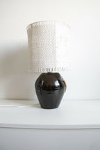 Lampe Puntia sur une table, abat-jour blanc cylindrique et base noire brillante