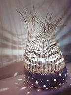 Lampe à poser tressée sombre sur base blanche à pois, fibres verticales au sommet.