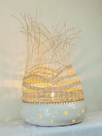 Lampe à poser en tressage clair, base blanche à pois, brins jaunes au-dessus.