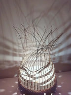 Lampe à poser en tressage sombre, base blanche à pois, fibres verticales au sommet.