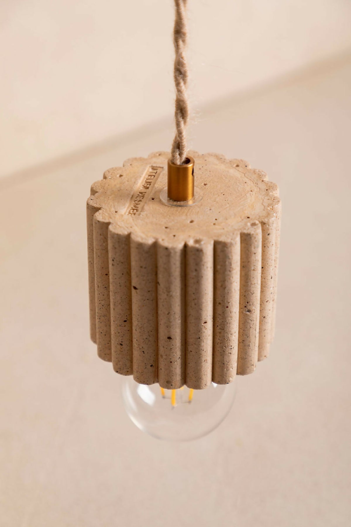 Suspension à abat-jour en ciment beige côtelé, vue rapprochée avec ampoule