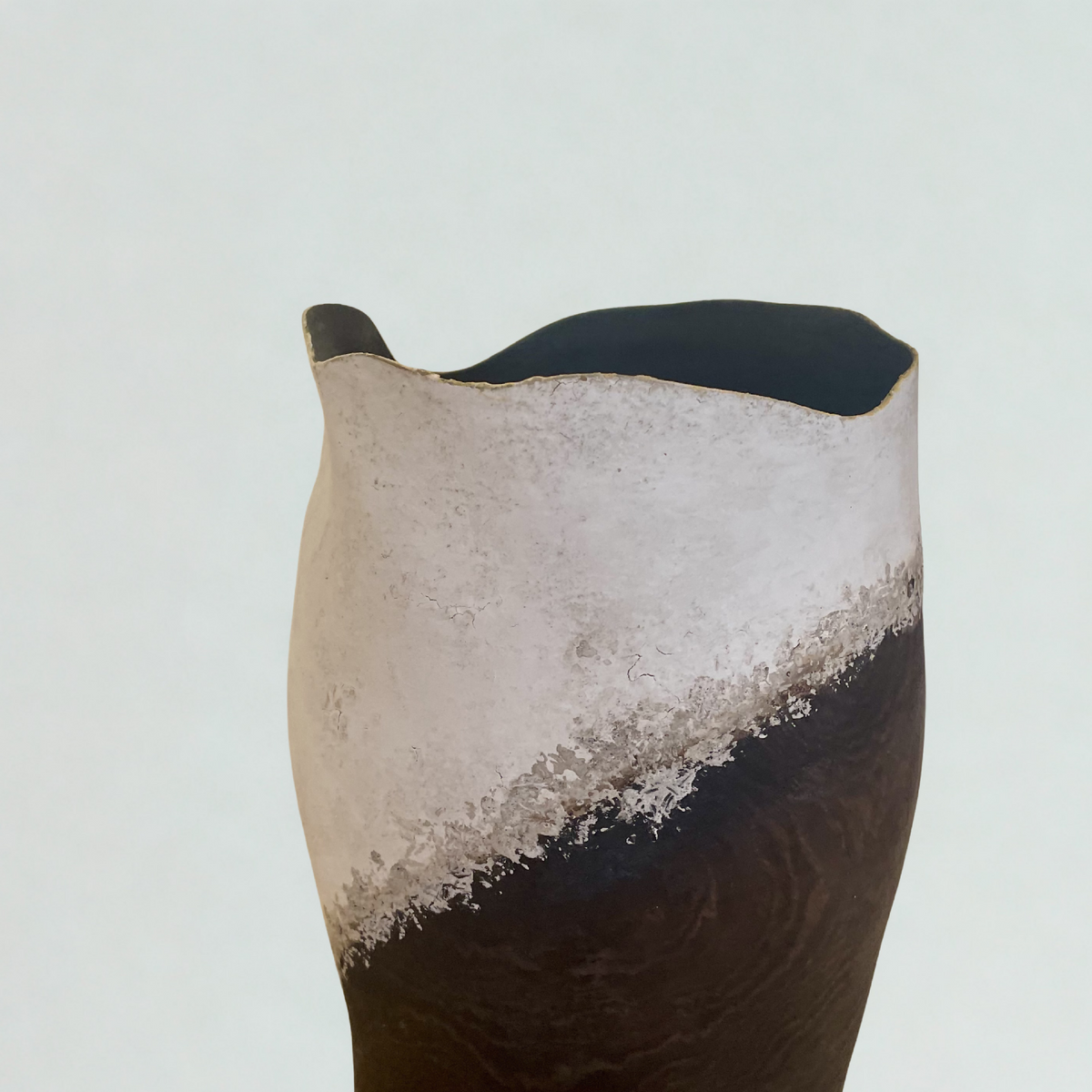 Vase en céramique noir et clair, ouverture échancrée sur le dessus, surface texturée