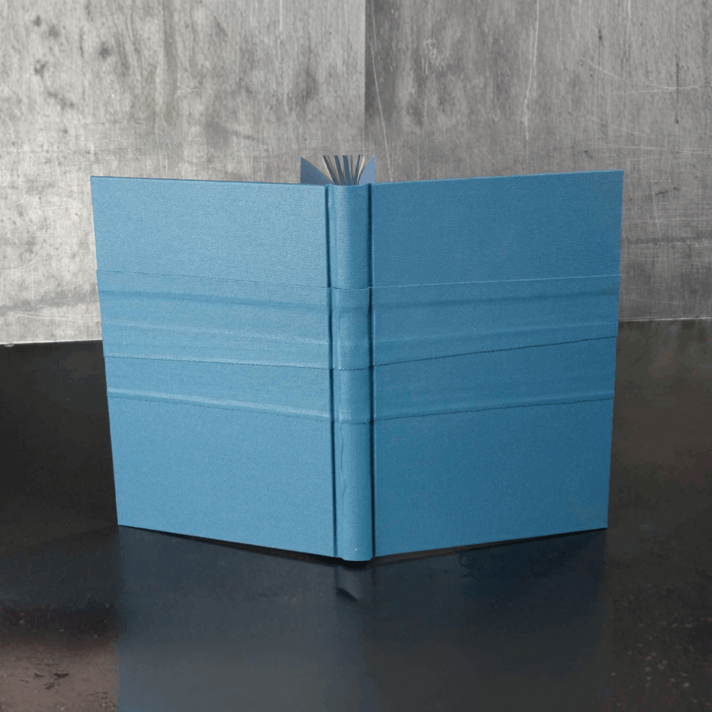 Livre d’or bleu, couverture ouverte en V avec marque-page et pages visibles.