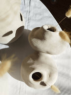 Peluche décorative blanche avec gros museau et yeux noirs, touffes beige dépassant du tissu.
