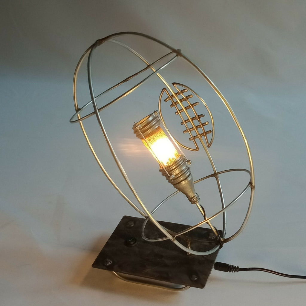 Lampe RUGBY allumée : cage métallique dorée, ampoule visible, base noire