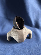 Petit pot en pierre gris avec ouverture ronde, intérieur sombre et bords irréguliers.