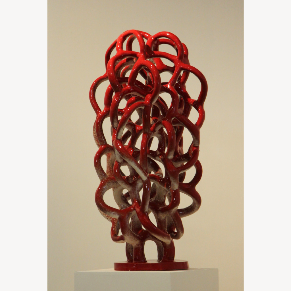 Sculpture abstraite de nœuds métalliques rouges, vue de face, sur socle.