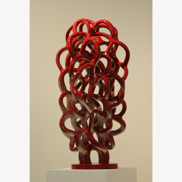 Sculpture abstraite de nœuds métalliques rouges, vue de face, sur socle.