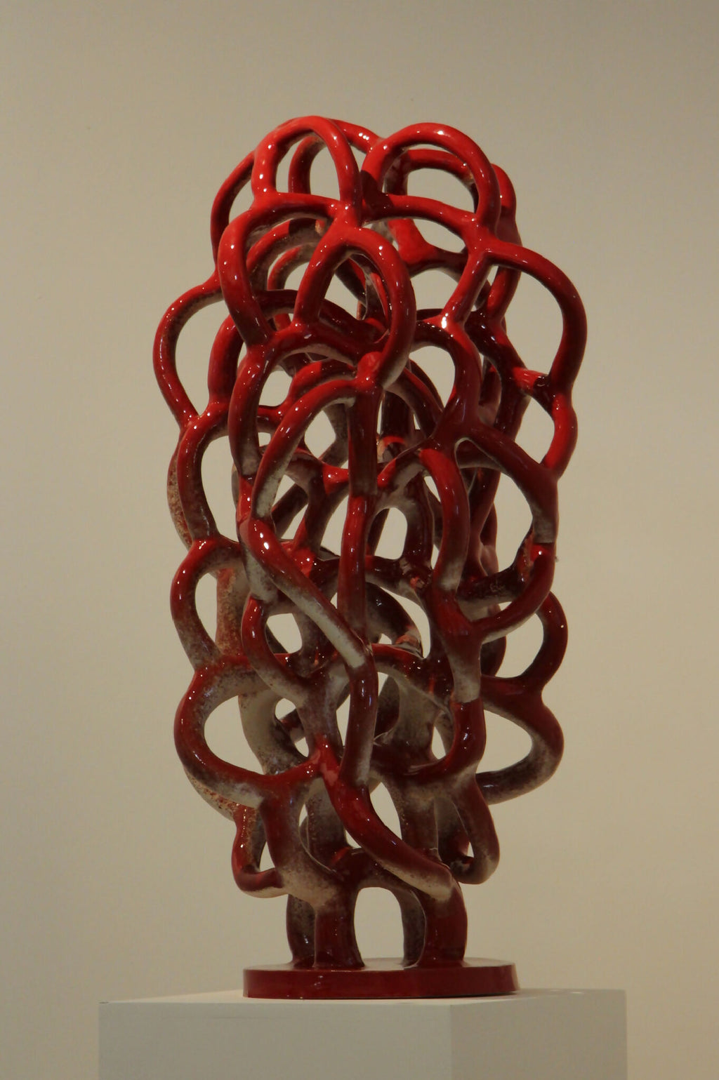 Sculpture décorative abstraite en nœuds de métal rouge sur socle blanc.